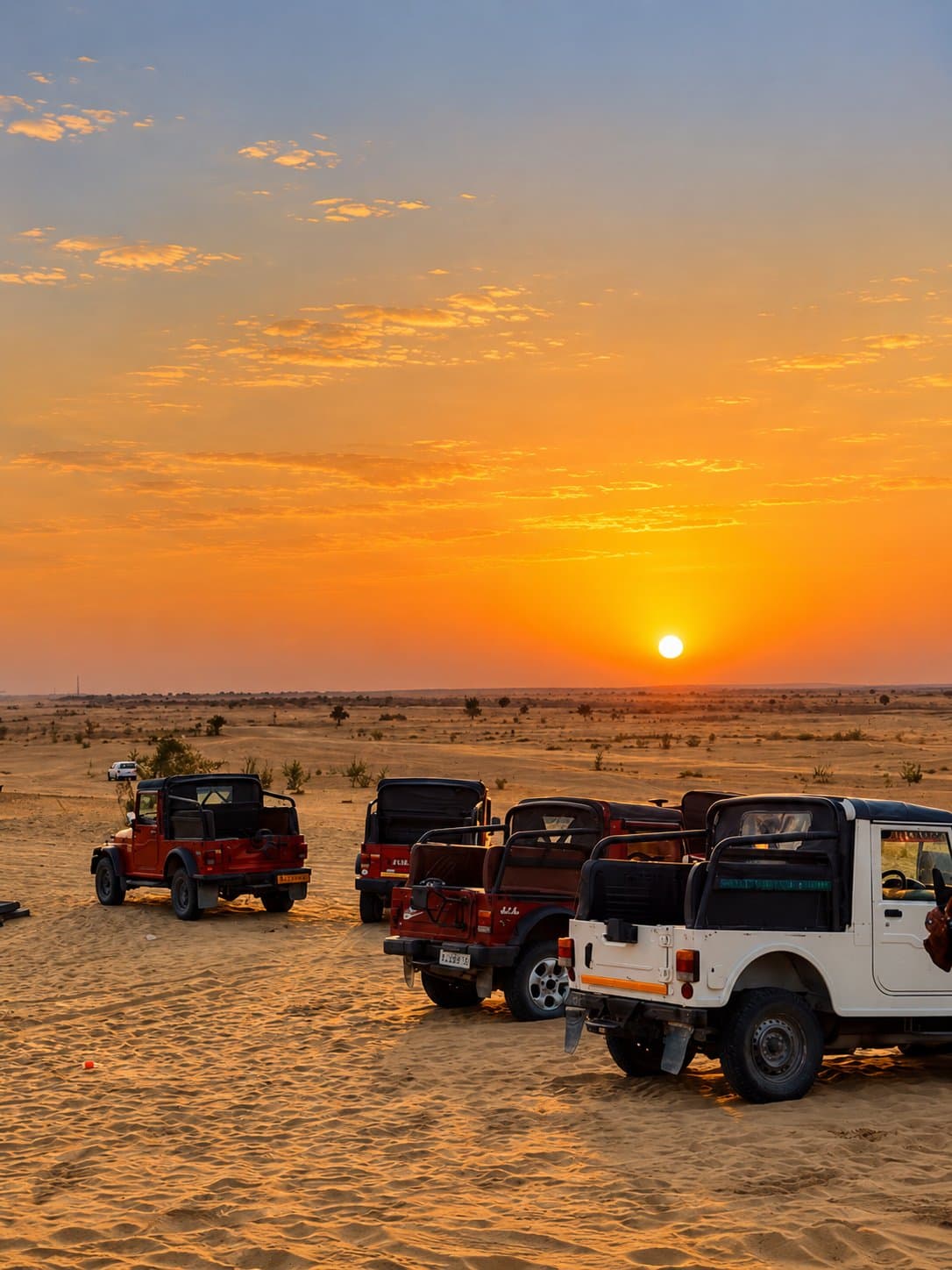 Open-top safari jeeps parked on the sand in the Thar Desert as the sun sets