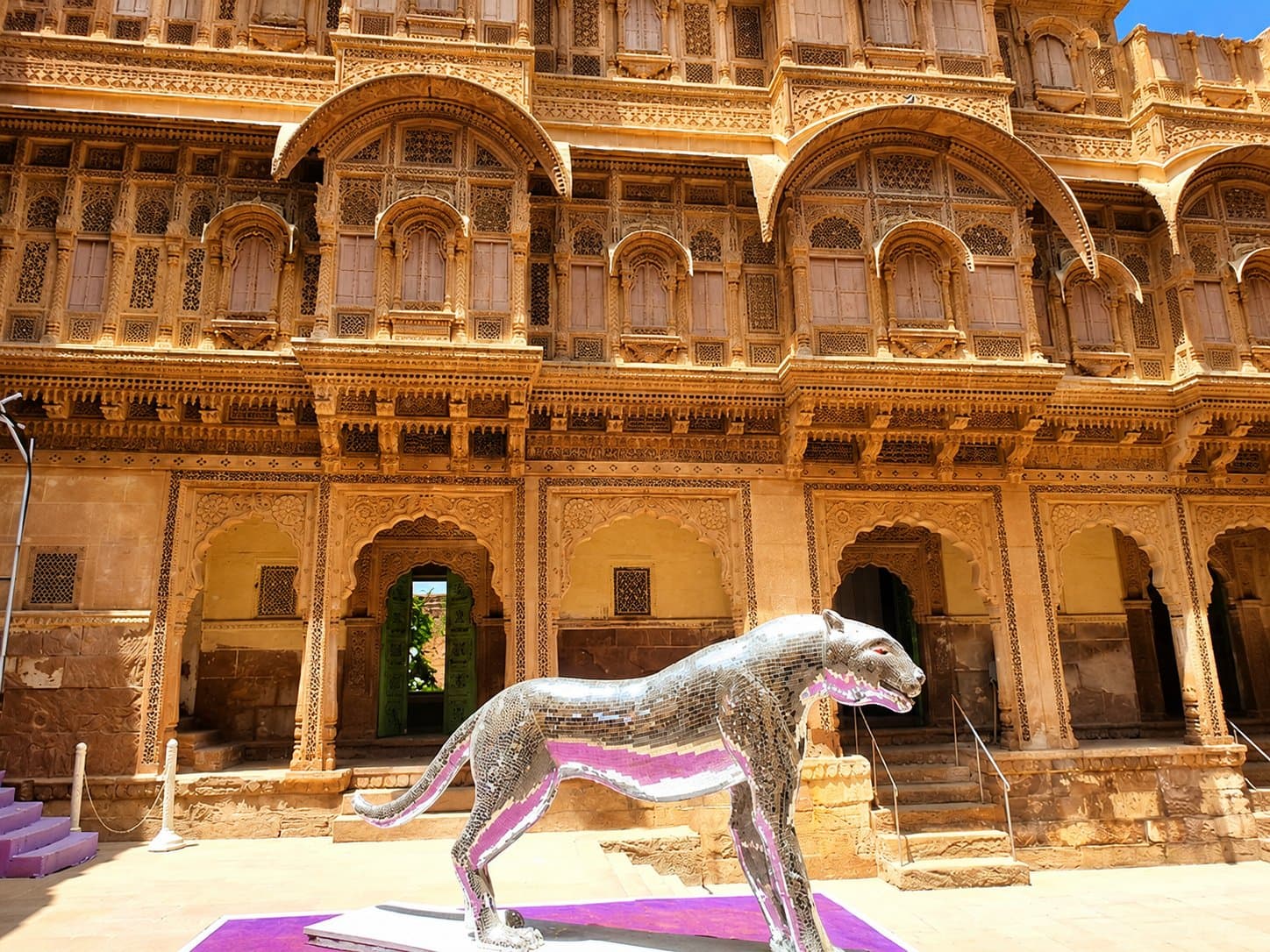 A palace courtyard of intricately carved sandstone balconies and arches, with a mirror-mosaic leopard sculpture in front