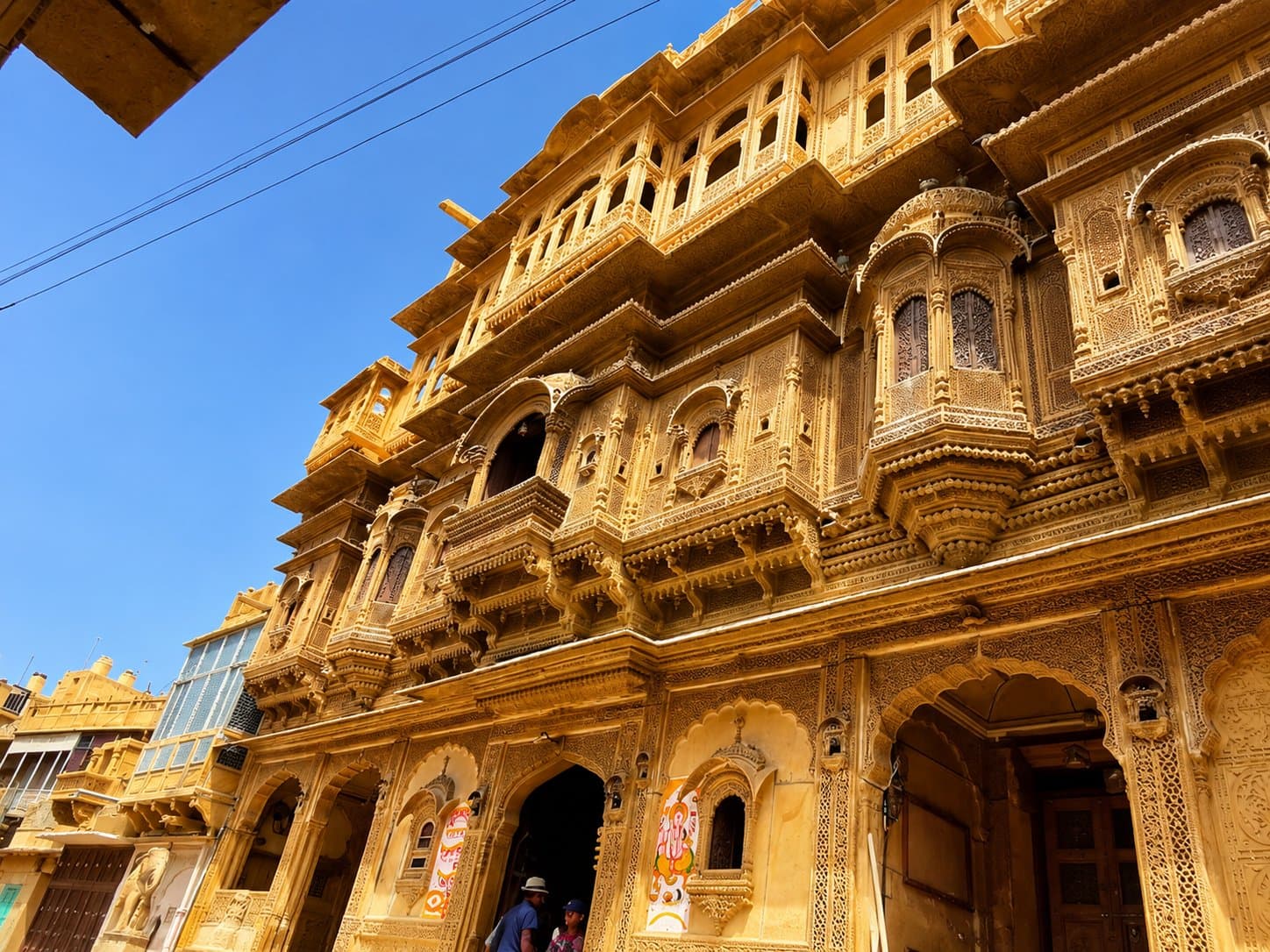 The carved golden-sandstone facade of Nathmal Ji Ki Haveli, looking up past its balconies to a blue sky, with a stone elephant by the entrance