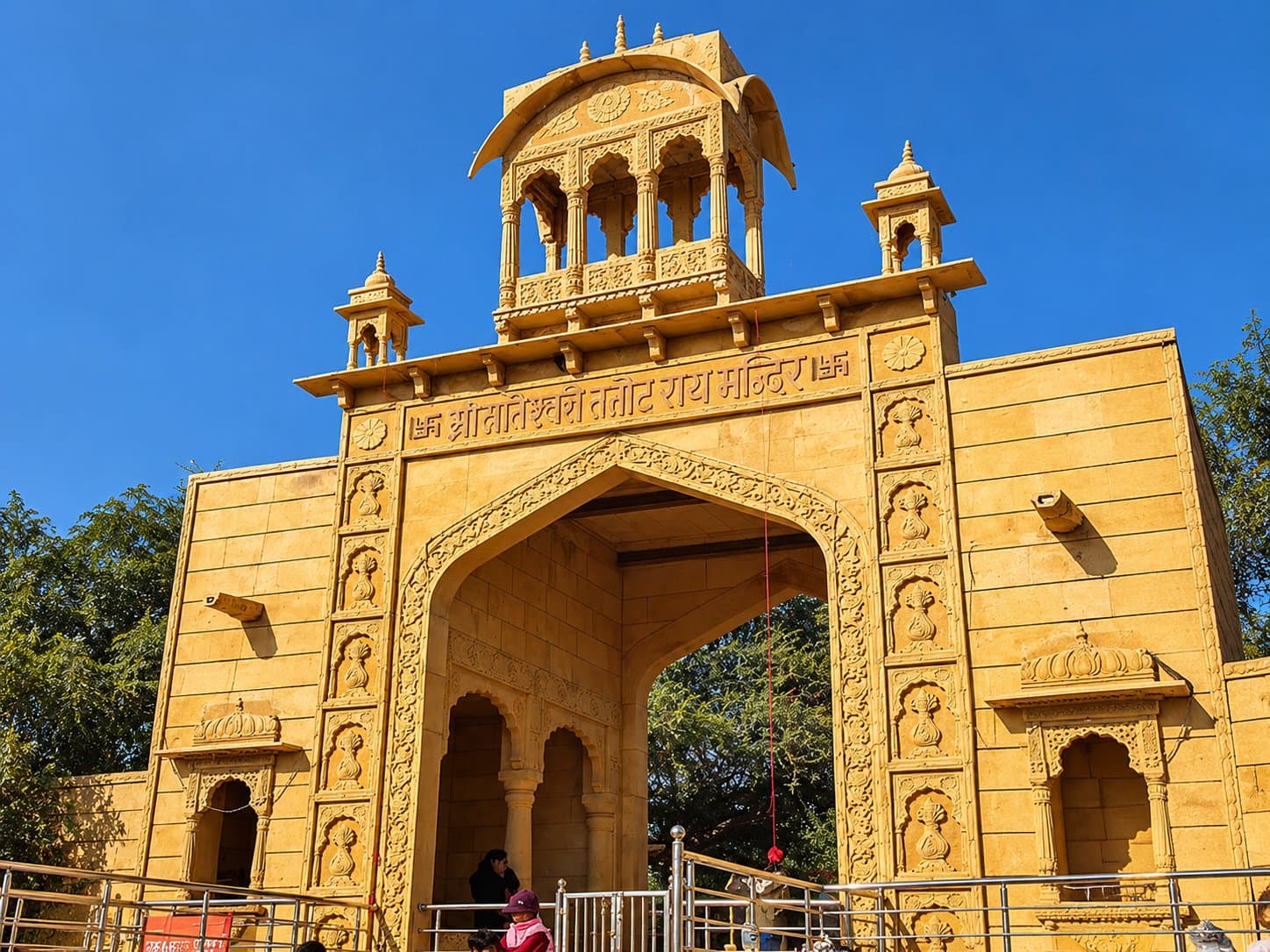 The carved sandstone entrance gate of Tanot Mata Temple, with its name inscribed in Hindi, under a clear blue sky
